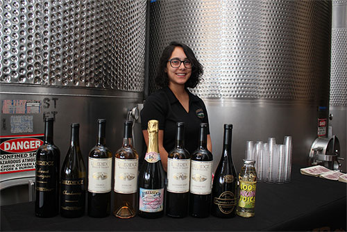 Young woman at a table displaying multiple wine bottles