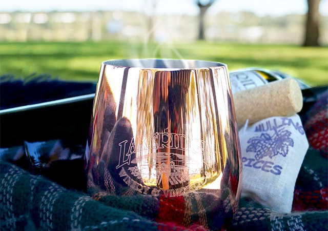 Mulled wine in a copper wine glass with bags of mulling spice next to it in an outdoor setting.